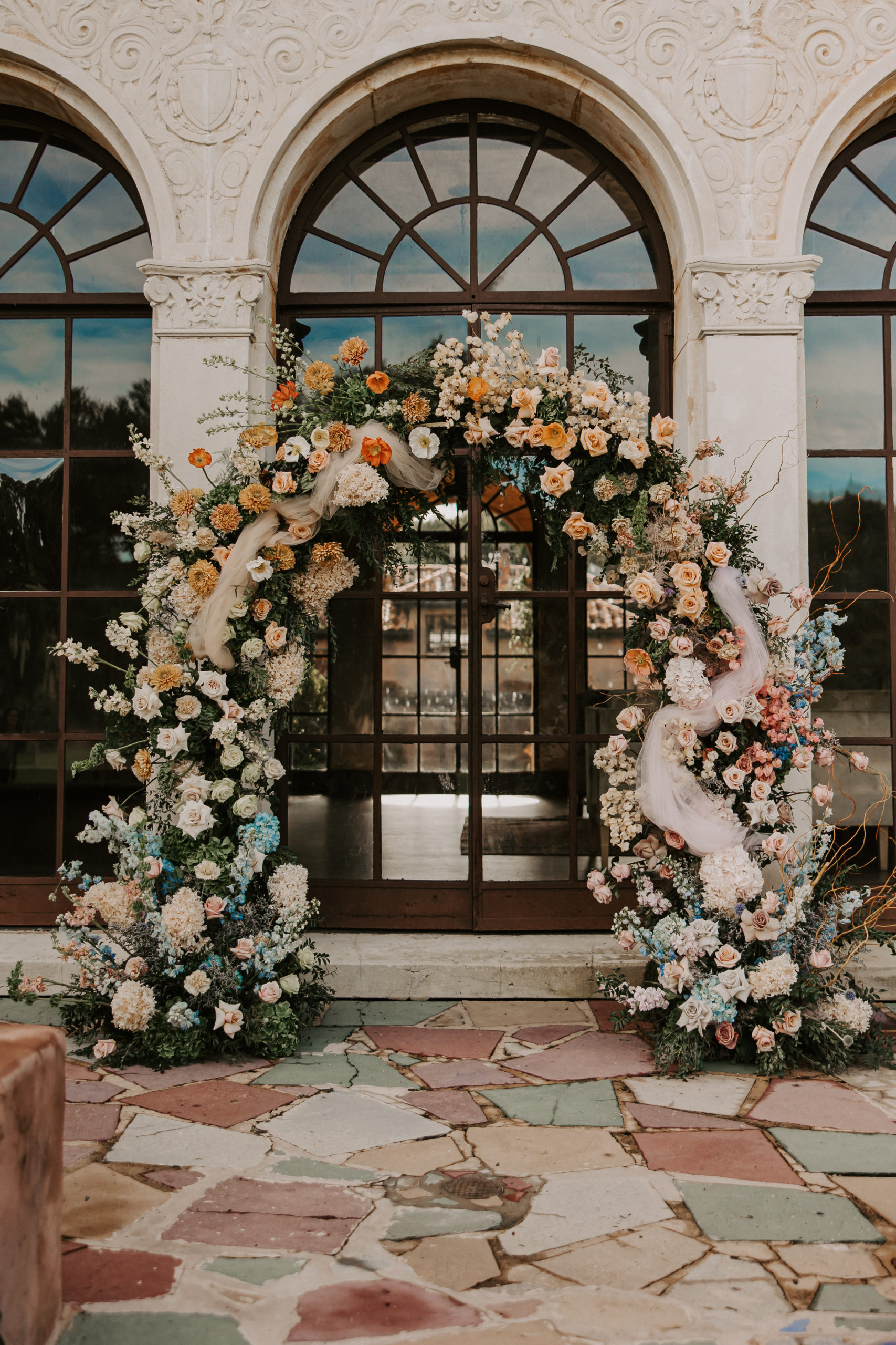 Jonathan took this inspiration and ran with it to create a beautiful muted rainbow floral arch.
Instead of using a traditional arch for the ceremony, our florist used over 40 types of blooms/floral to create an 8 foot tall massive rainbow arch which joins the array of colorful taper candles.